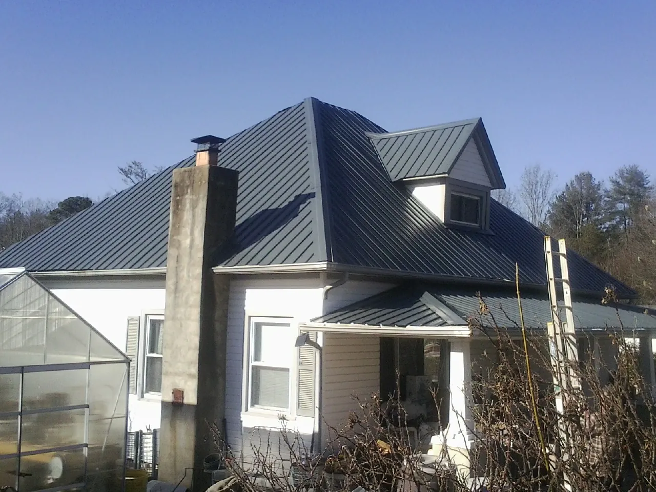 Dark blue standing seam metal roof on a white farmhouse with dormer — Slate & Tile Roof Repair by Roofing Brothers in Waddell