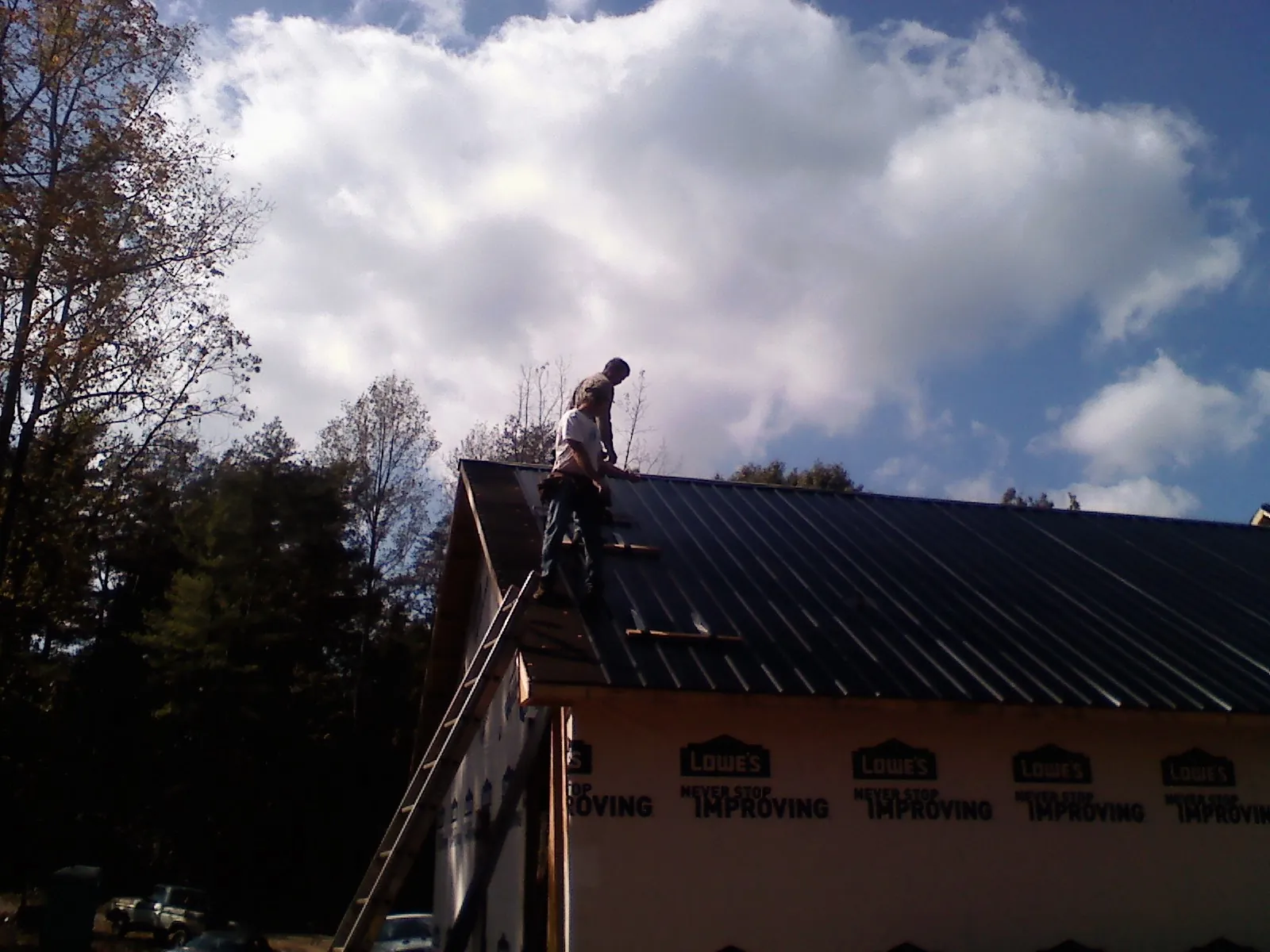 Roofer fastening dark metal panels high against a cloudy sky, from a Roof Inspection job in Waddell
