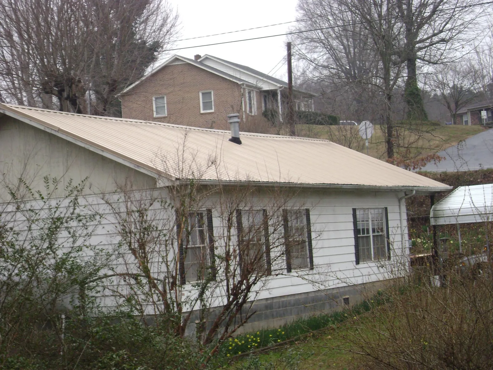 Tan metal roof on a white sided house set into a hillside — Commercial Roofing by Roofing Brothers in Waddell